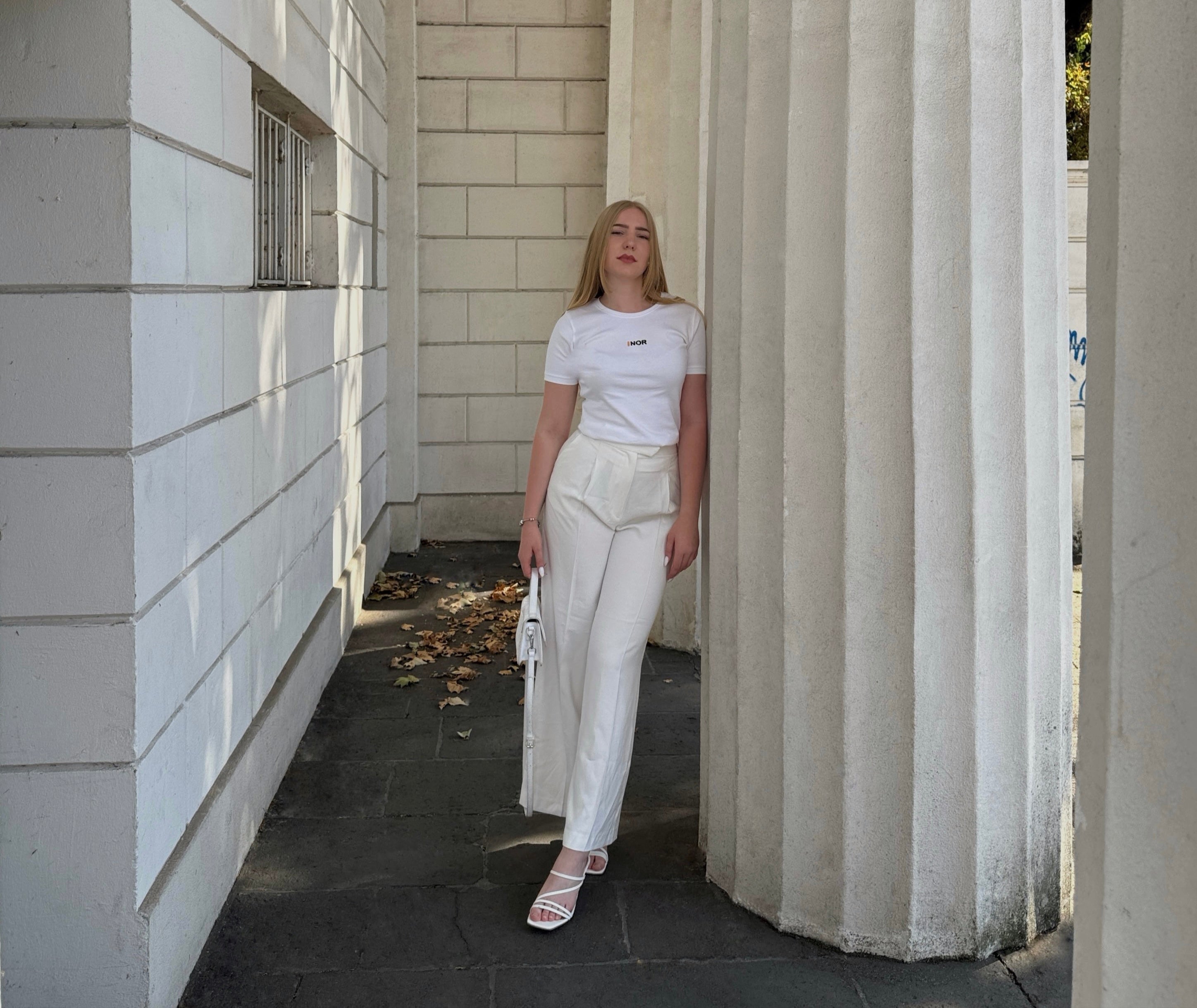 Woman in a white outfit wearing the F1 signature tee standing in a sunlit architectural setting with columns.
